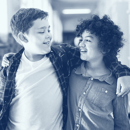 Zwei Jungs gehen Arm in Arm durch einen Schulflur und lächeln sich an.